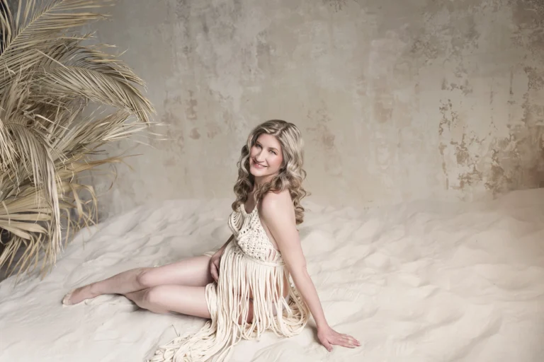 Állapotos hölgy makramé ruhában ül homokban, természetes fényű boho stílusú fotózáson