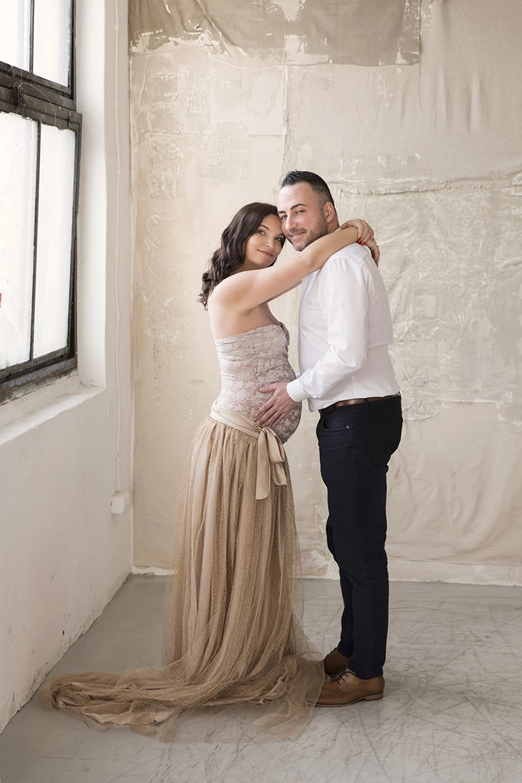 Kismama bézs ruhában áll apukával, romantikus kismama fotózás stúdióban