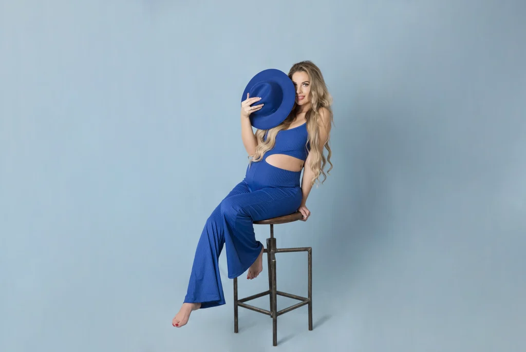 Kezdőlap Kismama kék overálban pózol kék háttér előtt, modern műtermi fotózás