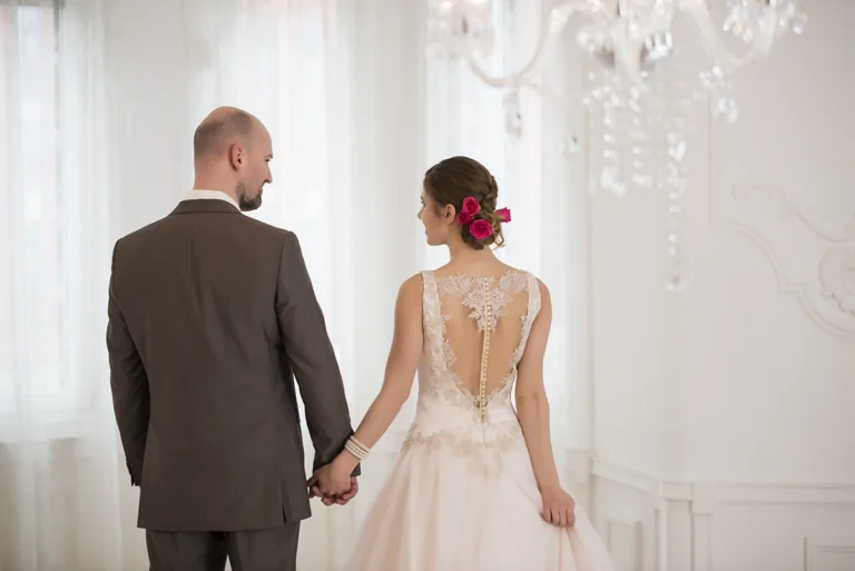 Menyasszony és vőlegény háttal állnak egymásnak, kezük összefonva, tekintetük találkozik
