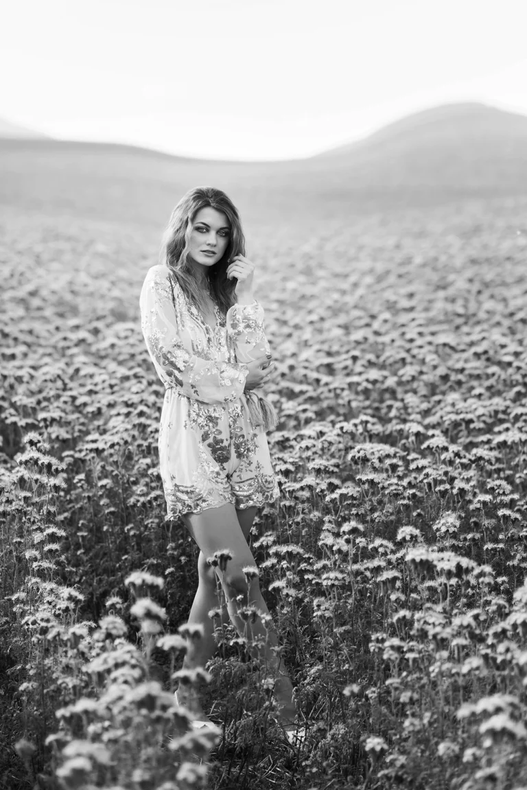Monokróm fotó fehér virágos mezőn álló hölgyről, elegáns és letisztult portré