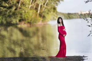 Kismama piros ruhában pózol a Duna partján, természetes kültéri fotózáson