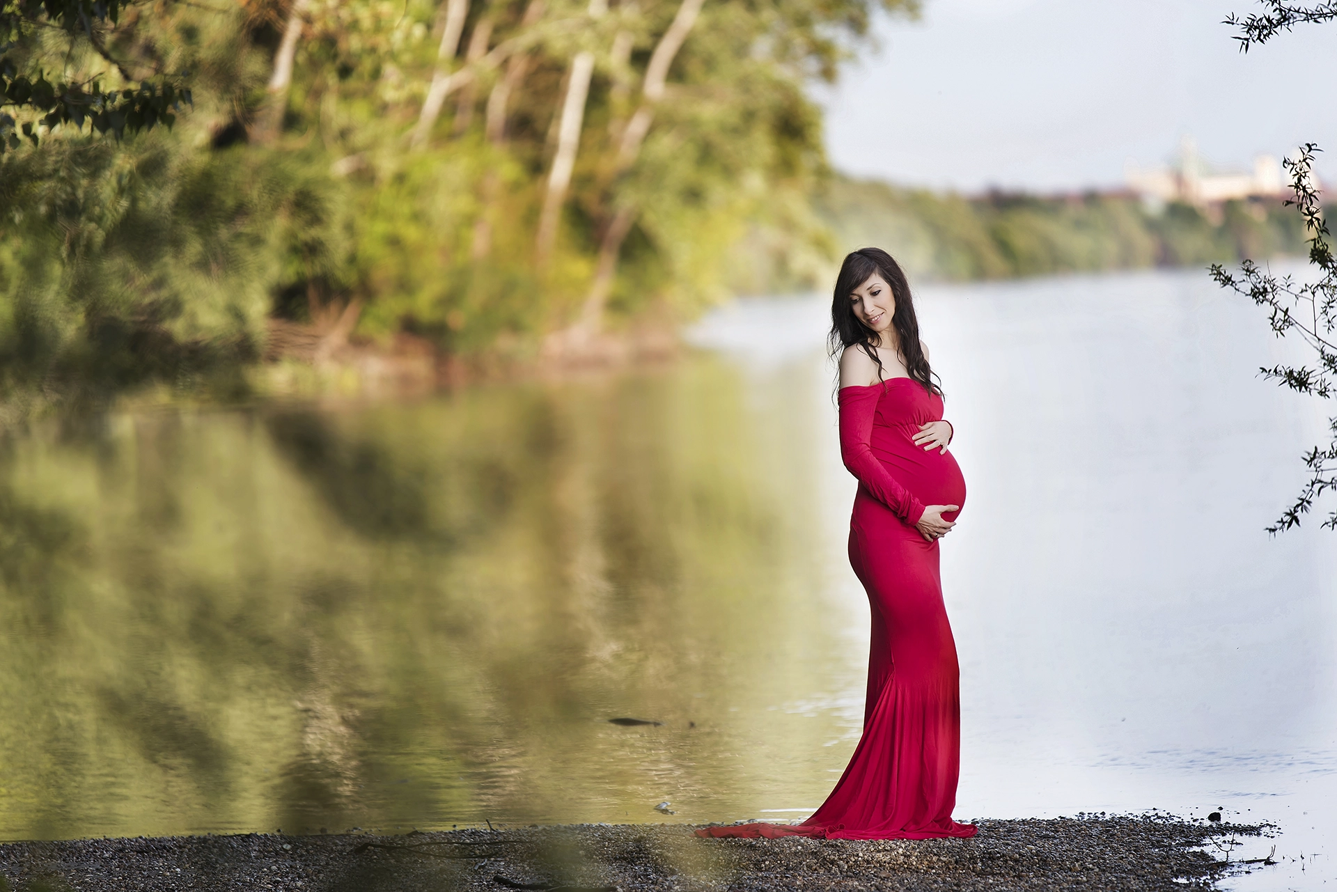Kismama piros ruhában pózol a Duna partján, természetes kültéri fotózáson
